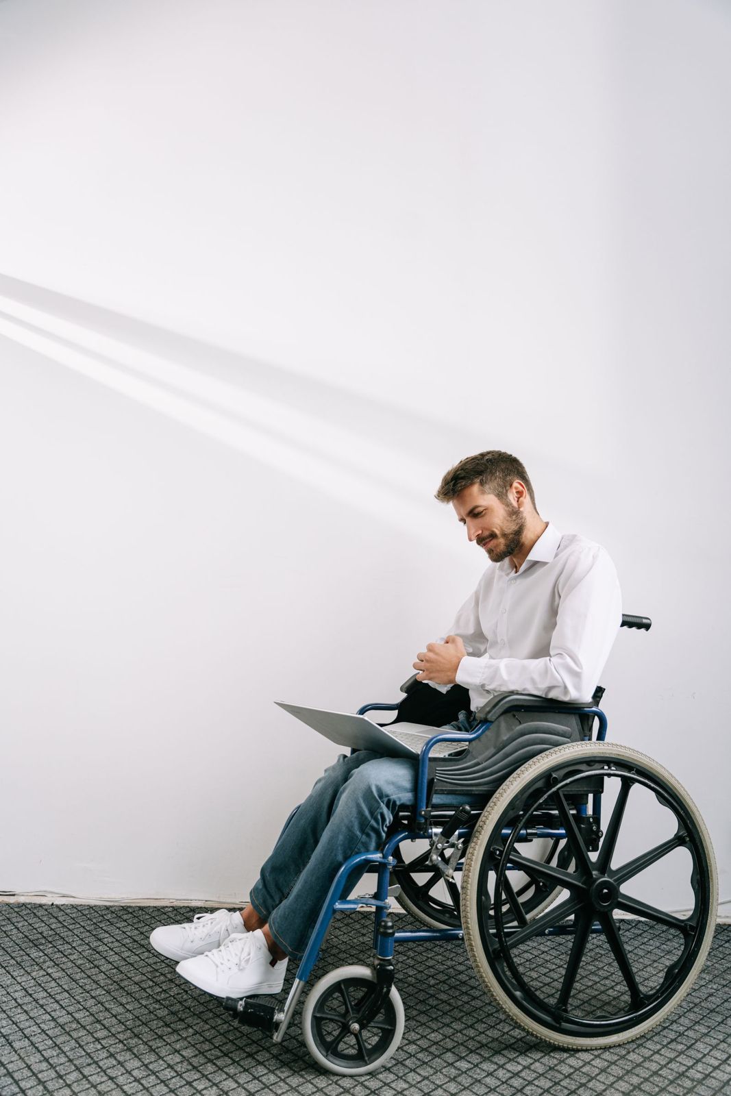 A man using a wheelchair works on a laptop in a bright room